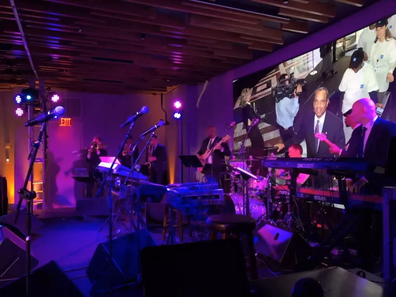 Live band performing with stage lighting, instruments, and a large video display